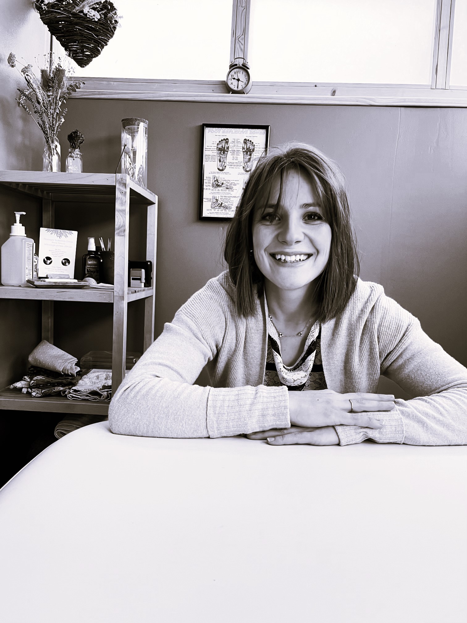 Portrait noir et blanc de Claire Missol dans son cabinet, assise derrière sa table de massage