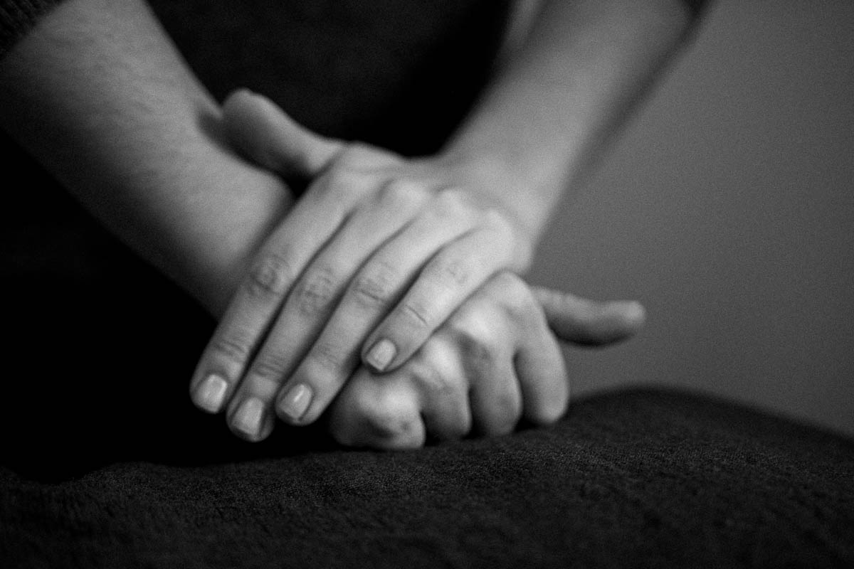 Gros plan sur les mains de Claire croisées au repos sur un tissu sombre, lumière latérale douce