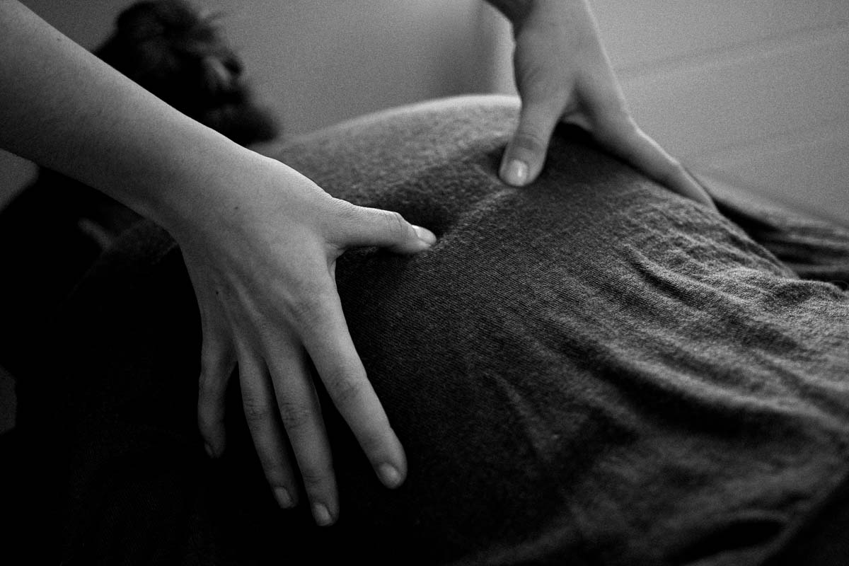 Les mains de Claire en train de masser le dos d’un patient à travers un pull en laine tricoté