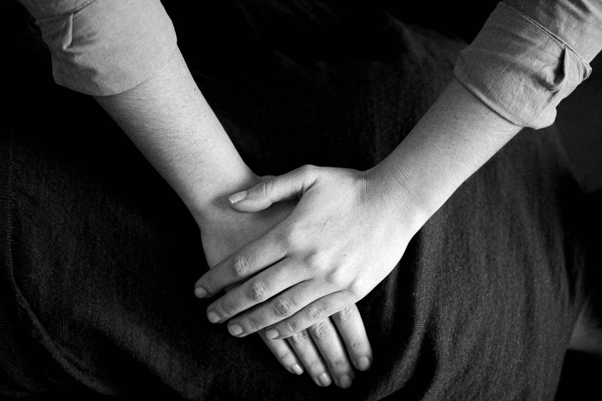 Gros plan noir et blanc sur les mains de Claire posées au repos, manches retroussées, sur un tissu de lin